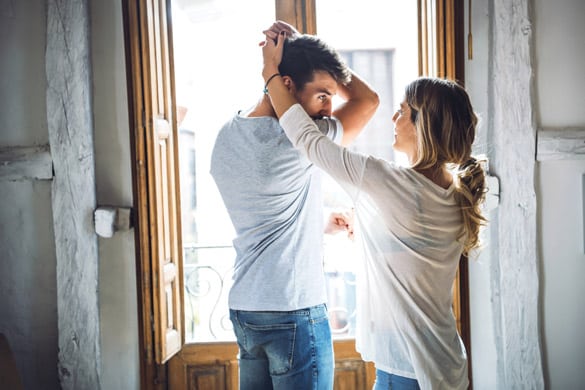 Happy young couple in casual outfits dancing in living room of apartment against big window - Are Virgo Men Secretive Sometimes