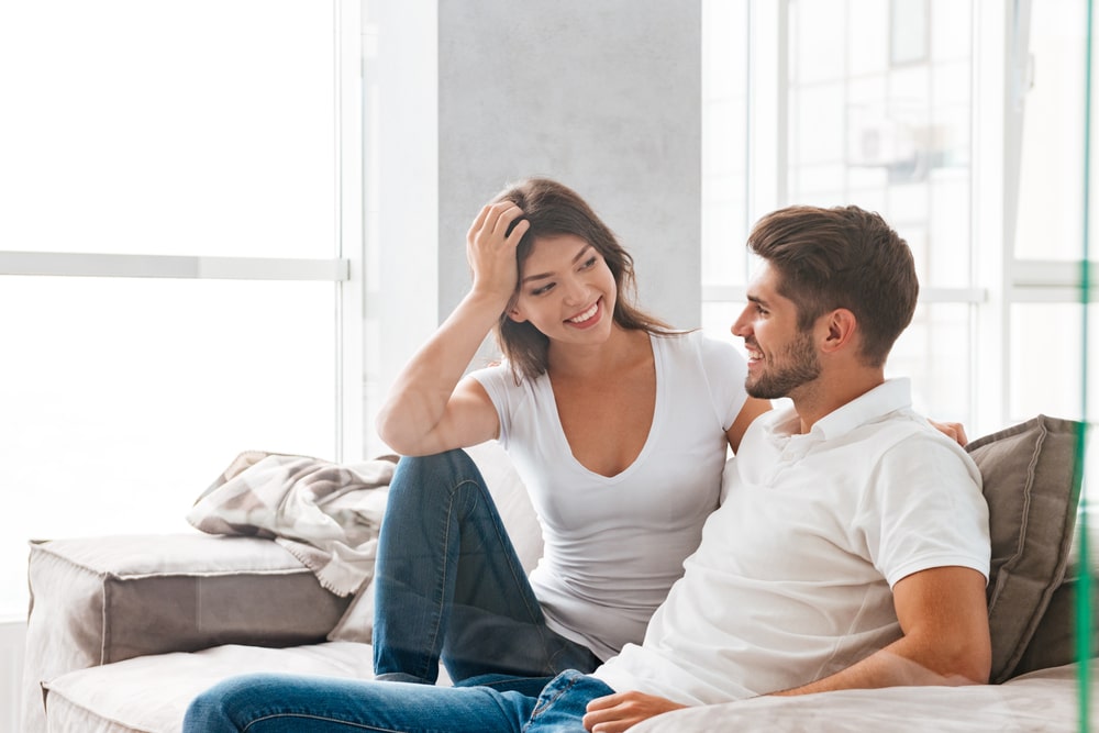 Cheerful beautiful young couple sitting and talking on sofa at home - Virgo Man Cancer Woman Problems